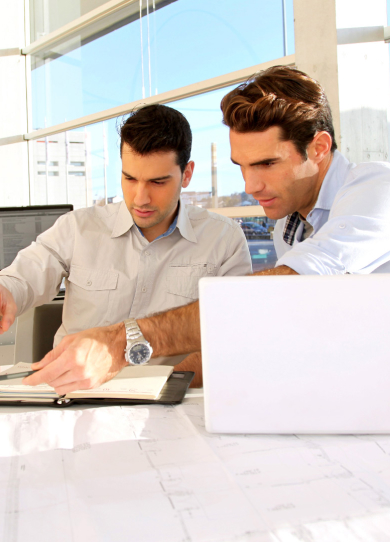 Dos compañeros de trabajo revisando documentos con sus computadores