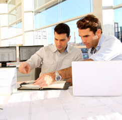 Dos compañeros de trabajo revisando documentos con sus computadores